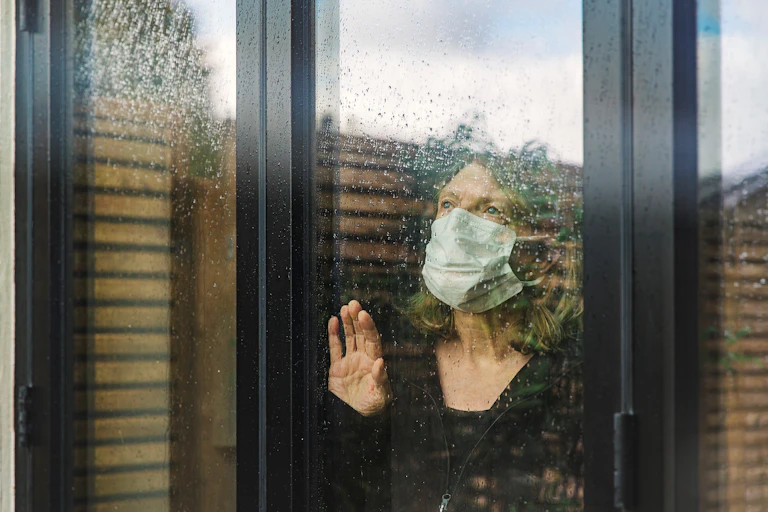 A senior woman, in isolation at home, looks out a window.