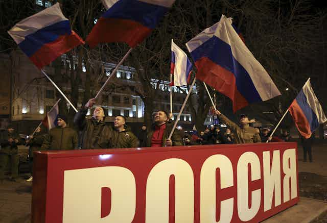 Joyous people waving flags during a nighttime gathering to celebrate recognition by Russia of the Eastern Ukraine breakaway republics.