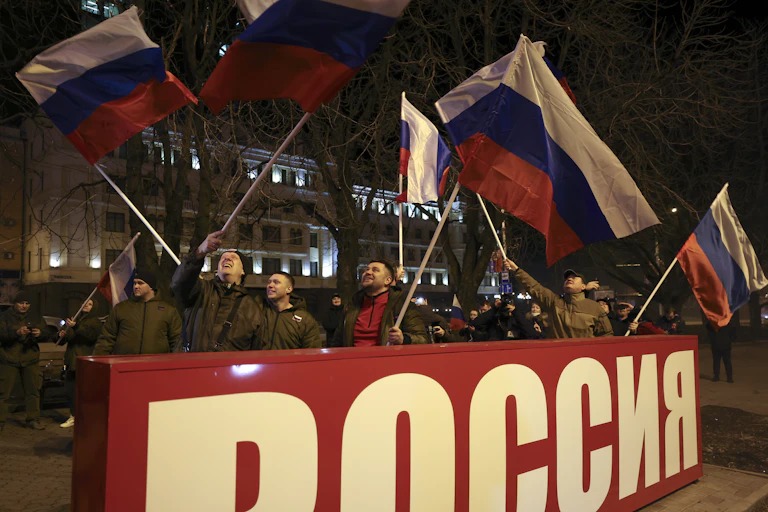 Joyous people waving flags during a nighttime gathering to celebrate recognition by Russia of the Eastern Ukraine breakaway republics.