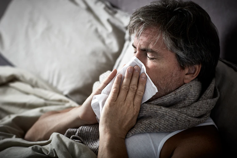 Man in bed blowing his nose.
