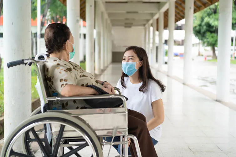 Carer talks to elderly person in wheelchair.