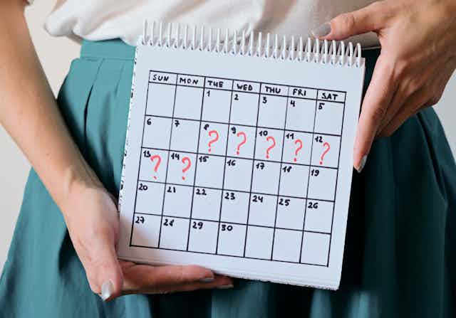 A woman holding a calendar with certain days annotated with question marks