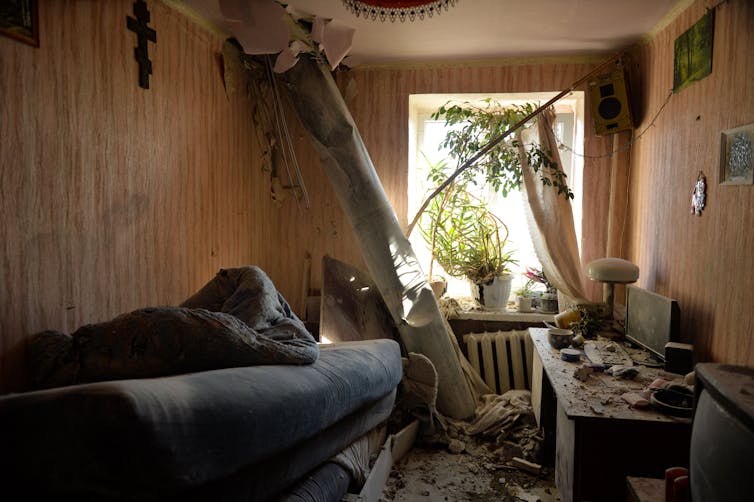 A rocket is stuck coming through the ceiling of a damaged apartment with rubble around it.