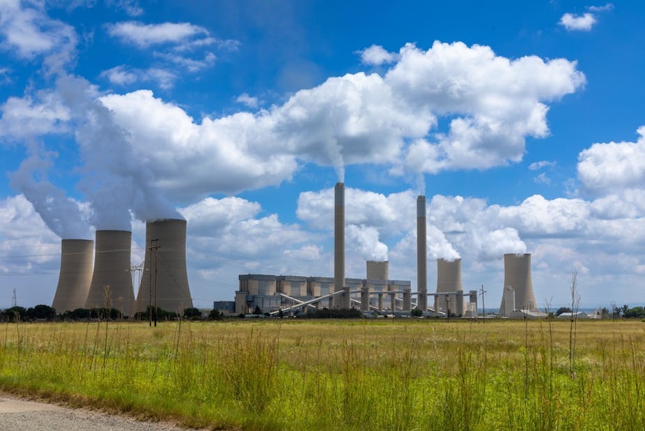 A coal fired power station in South Africa emitting smoky gas into the sky. There's a grass field in the foreground.