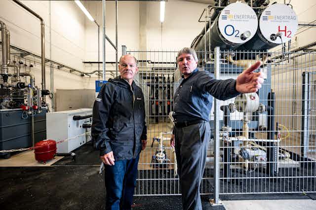 Dos hombres en el interior de una central eléctrica rodeados de maquinaria.