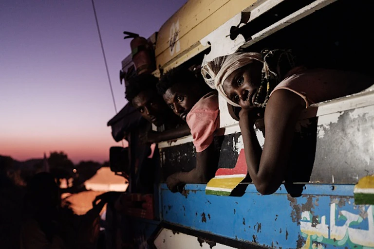 Three people lean from a moving vehicle