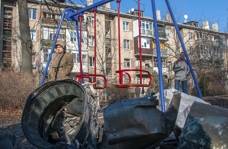 A man and woman stand in a playground looking at fragments of military equipment.