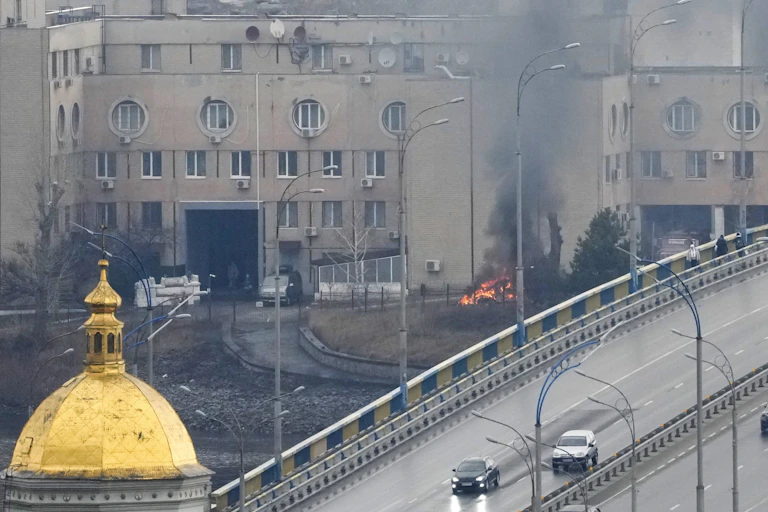 the golden dome of a church in the foreground with a fire burning behind it in front of a concrete building