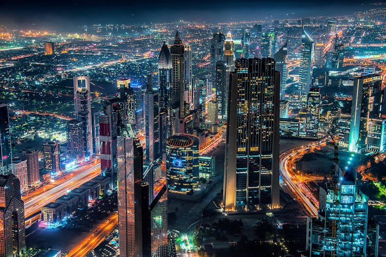 Skyline of a city at night, featuring highrise buildings and bright lights.