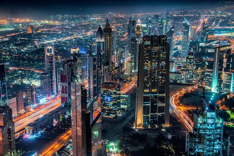 Skyline of a city at night, featuring highrise buildings and bright lights.