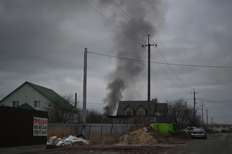 Smoke rising in a cloudy sky near small homes.