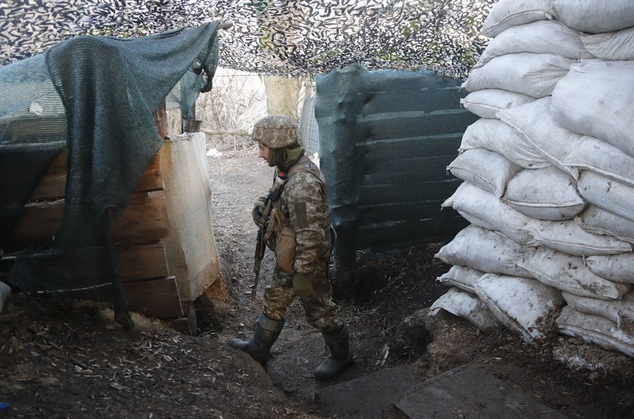 Ukrainian soldier patrolling in a fort or trench next to a large pile of white sandbags