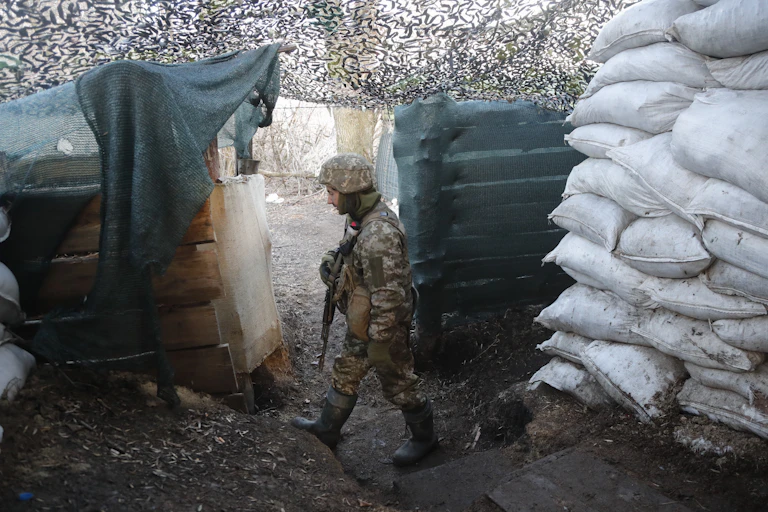 Ukrainian soldier patrolling in a fort or trench next to a large pile of white sandbags