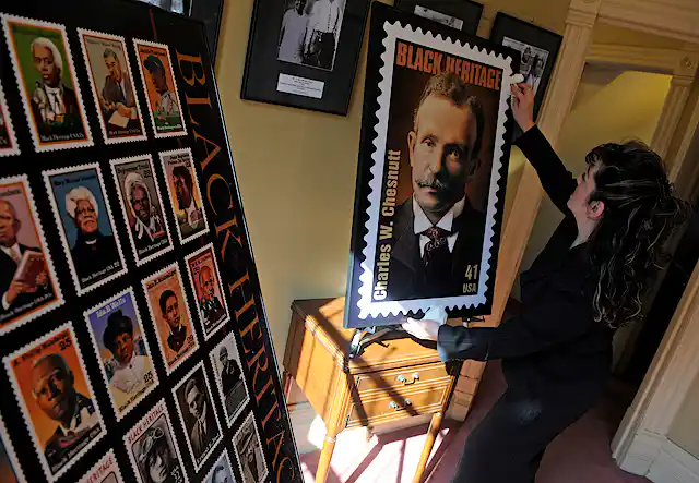 Woman holds enlarged stamp featuring portrait of man with mustache.