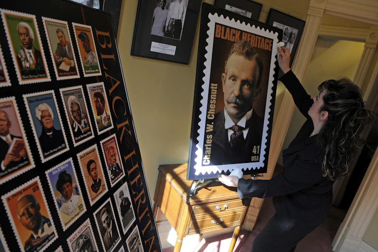 Woman holds enlarged stamp featuring portrait of man with mustache.