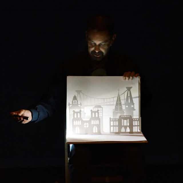 A man shines a torch on some small paper buildings