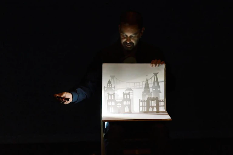A man shines a torch on some small paper buildings