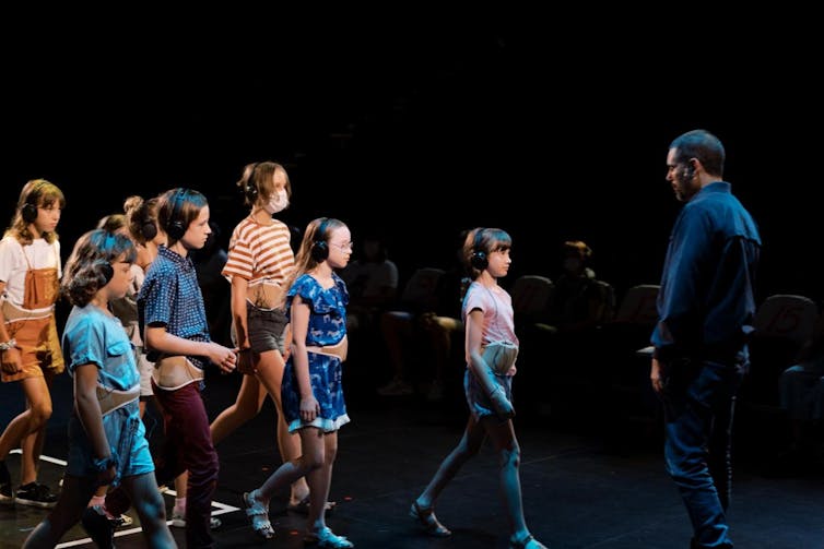 A group of children wearing headphones walk towards a man
