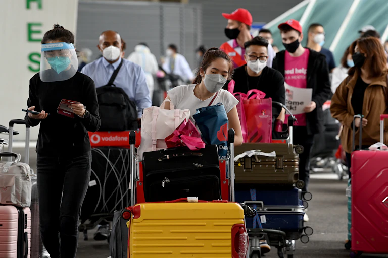 Masked students pushing baggage trolleys on arrival in Australia