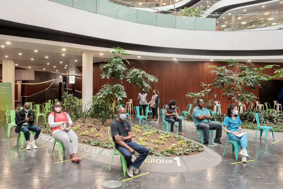 People wearing masks sitting on chairs in a line.