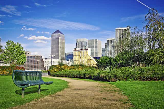 A green bench next to a winding park path with the City of London skyline in the distance.