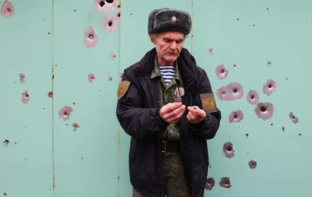 Ukranian male resident stands next to building damaged by shelling.