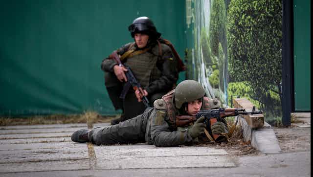 Two soldiers, one lying on his stomach pointing his weapon.