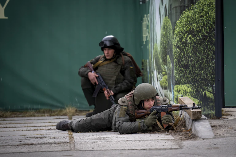 Two soldiers, one lying on his stomach pointing his weapon.
