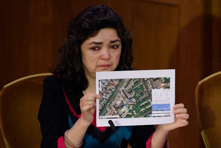 A woman has tears in her eyes as she holds up a satellite photograph