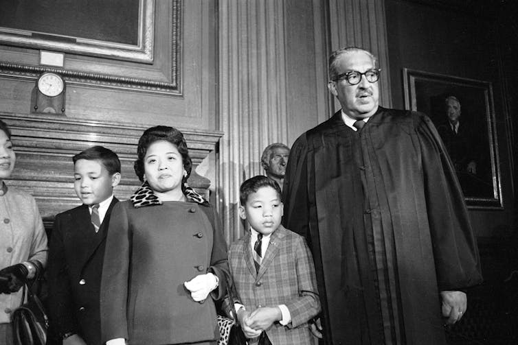 Uma foto em preto-e-branco mostra um homem negro alto em trajes da Suprema Corte com uma mulher formalmente vestida e crianças.