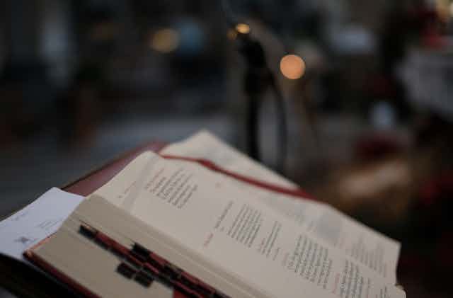 The Bible in church seen in profile in dim light, with red bookmarks and dark background.