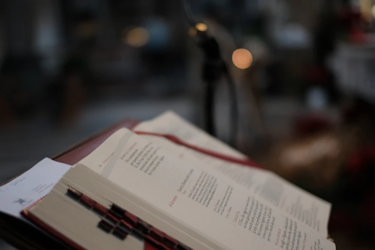 The Bible in church seen in profile in dim light, with red bookmarks and dark background.