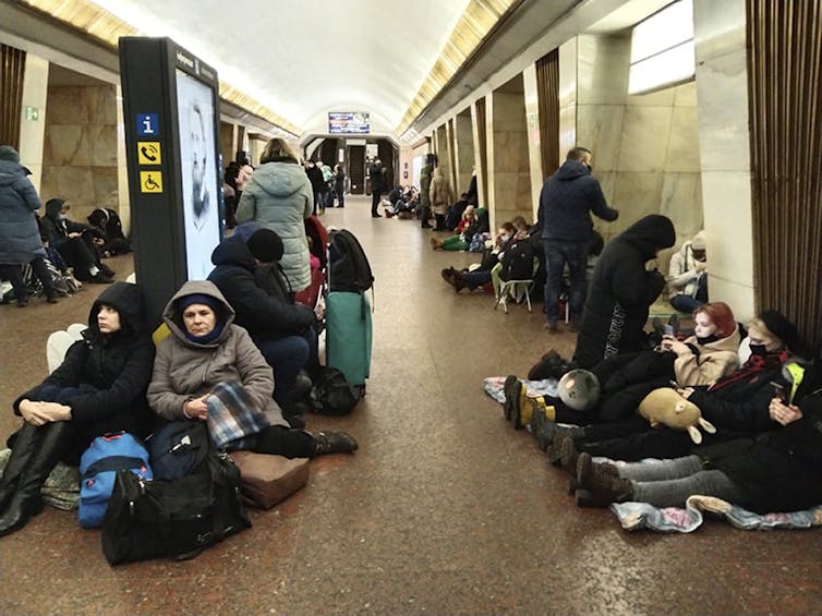 Groups of people are huddled throughout a subway platform.