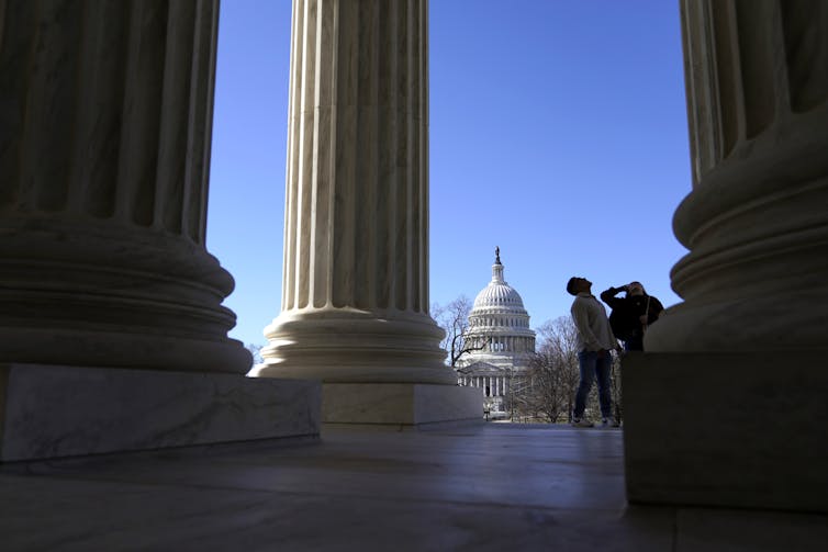 The U.S. Capitol is seen through columns on the outside of the Supreme Court.