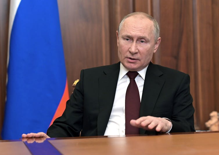 Putin at a desk with the Russian flag in the background