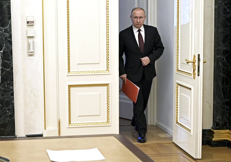 A man in a suit walks past a set of large ornate doors.