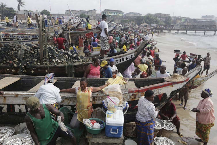 A beach packed with boats, with fishers and people sorting and buying fish.