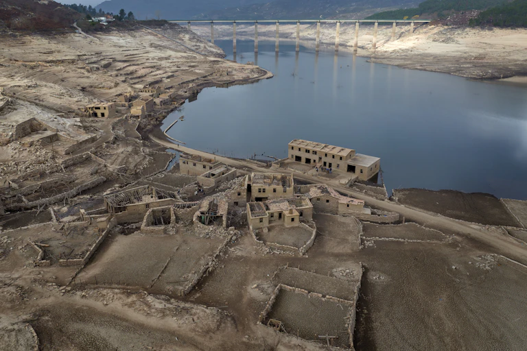 Abandoned buildings, foundations and a road standing next to a reservoir.