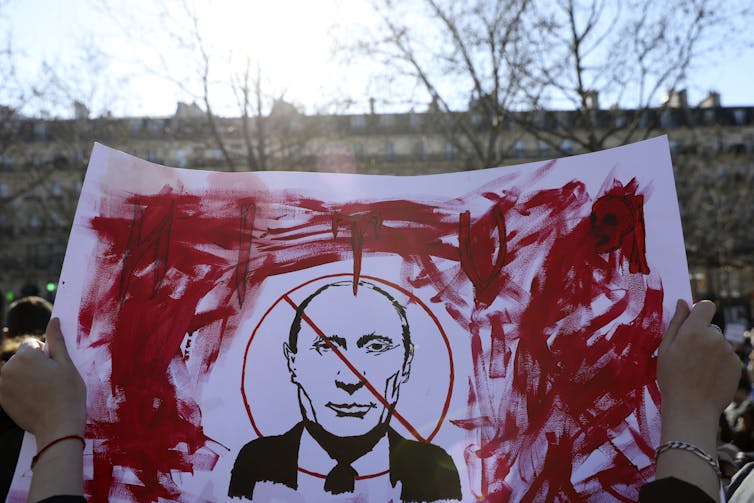 A poster covered in red marker shows Vladimir Putin's face with a red line through it.