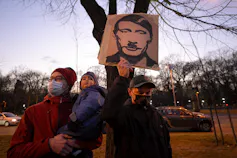 A man holds a placard depicting Vladimir Putin as Adolf Hitler.