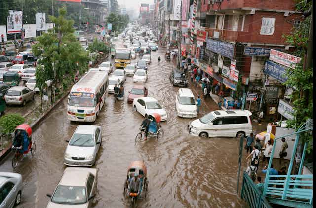 Cars, pedicabs and commuters on foot navigate flooded streets.