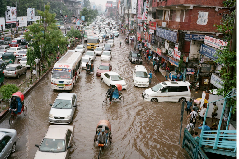 Cars, pedicabs and commuters on foot navigate flooded streets.