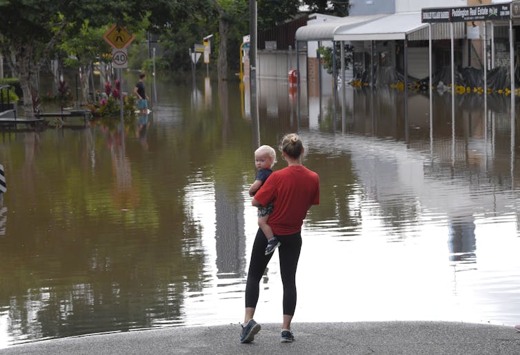 woman holds small child with flood waters in background