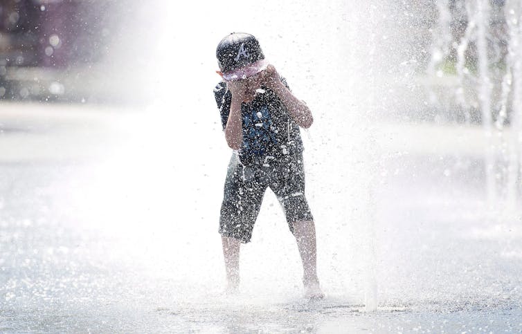 A boy protects his eyes from the upward spray of the fountain.