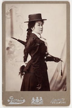 woman standing with umbrella, side on, wearing hat