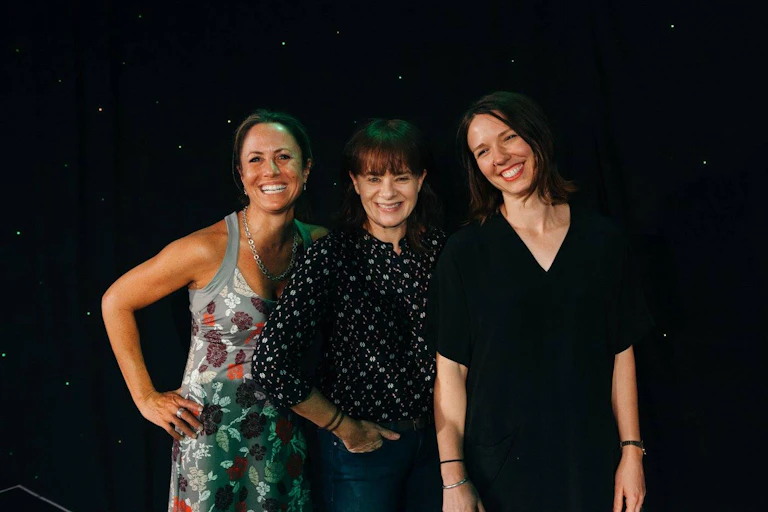 three women smiling together on a stage