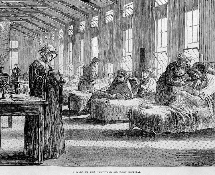 Old illustration of a large room with a row of patients in beds and nurses looking after them