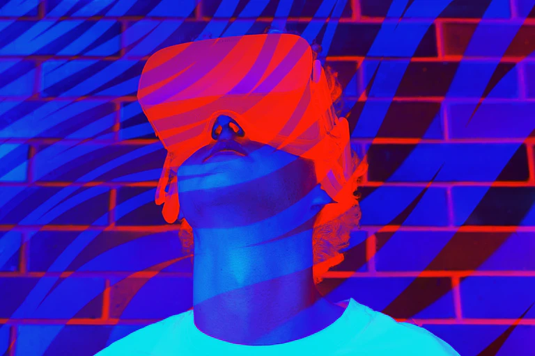 A young man or teenager in a white t-shirt wears a virtual reality headset with fluorescent blue, purple and orange colors in the background.