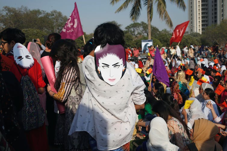 A crowd of people with flags and masks in the sun.