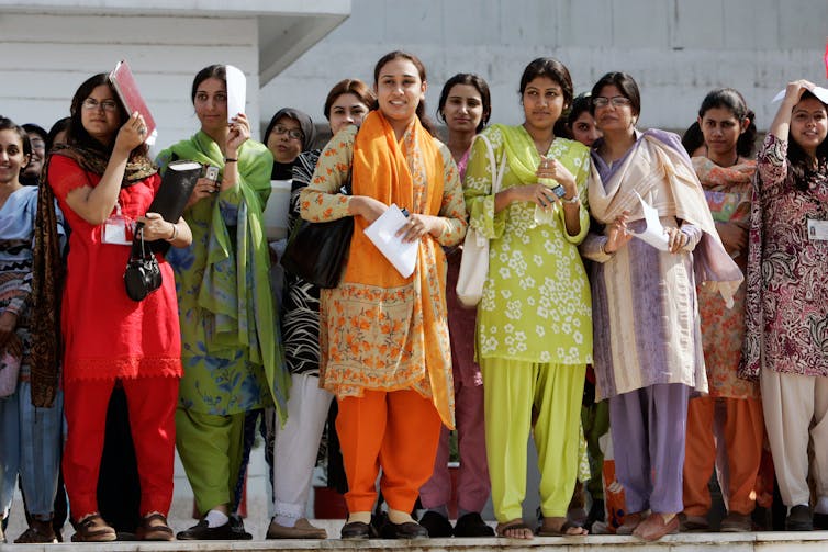Women in colourful salwar kameez stand in a group in the sun.